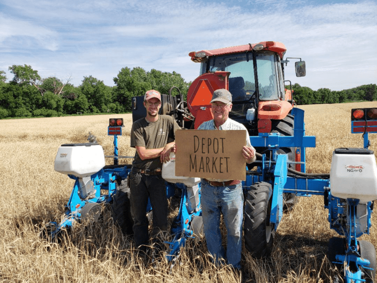 two men holding a depot market sign in front of a tractor in a field