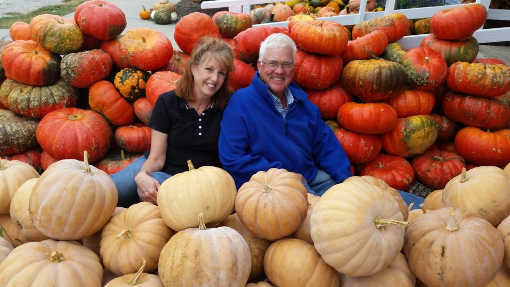 man and woman sitting in a pile of pumpkins