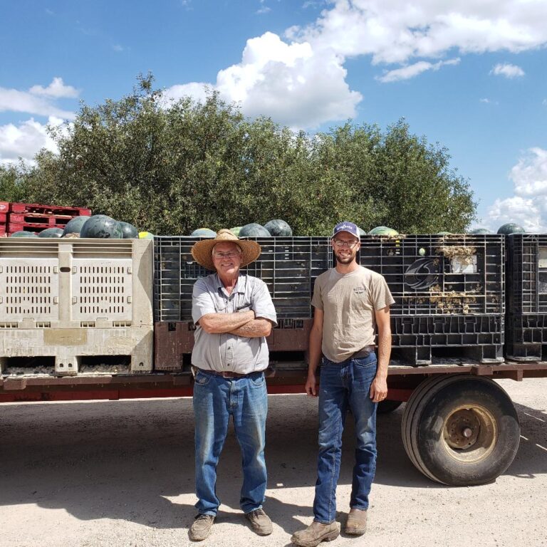 two men standing in front of a produce truck